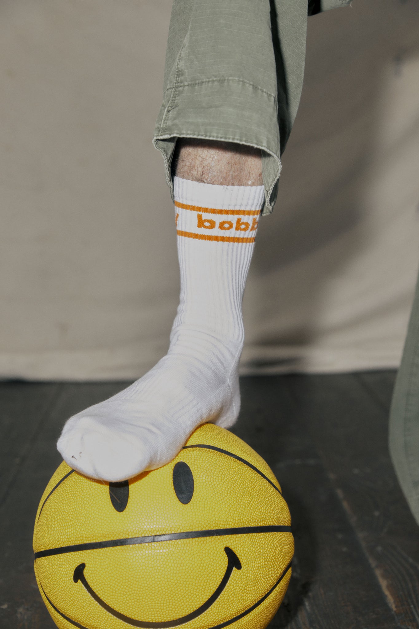 mans foot wearing white and orange branded socks while standing on a smiley face basketball
